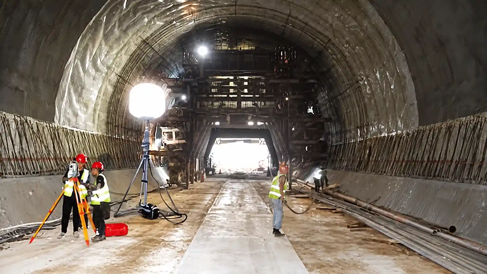 Tunnel under construction lit by a tripod balloon light, two workers in high visibility vests in the foreground