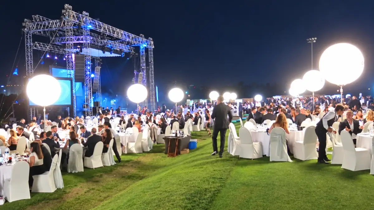 Outdoor evening event with several balloon lights glowing above tables on a lawn